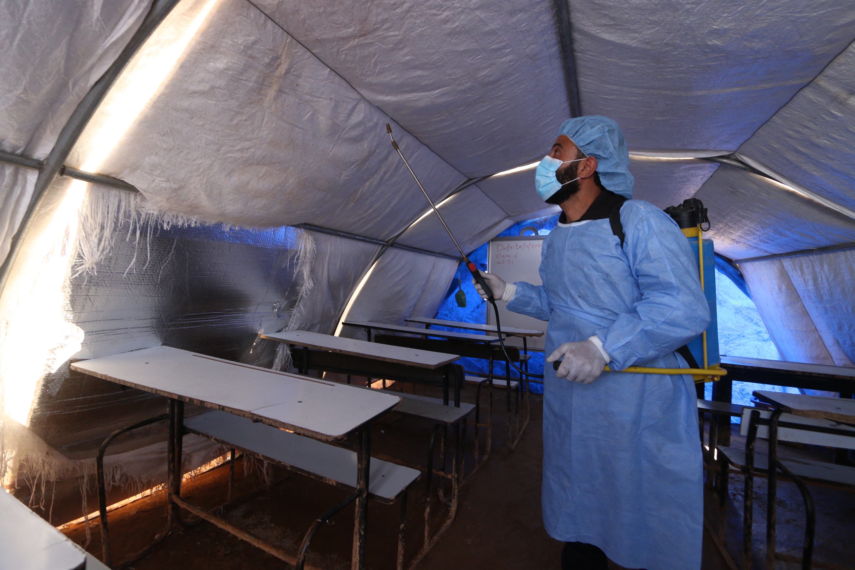 عمال الإغاثة في مخيم أطمة للاجئين يقومون برش مطهر على الأسطح لمنع انتشار فيروس كوفيد-19.