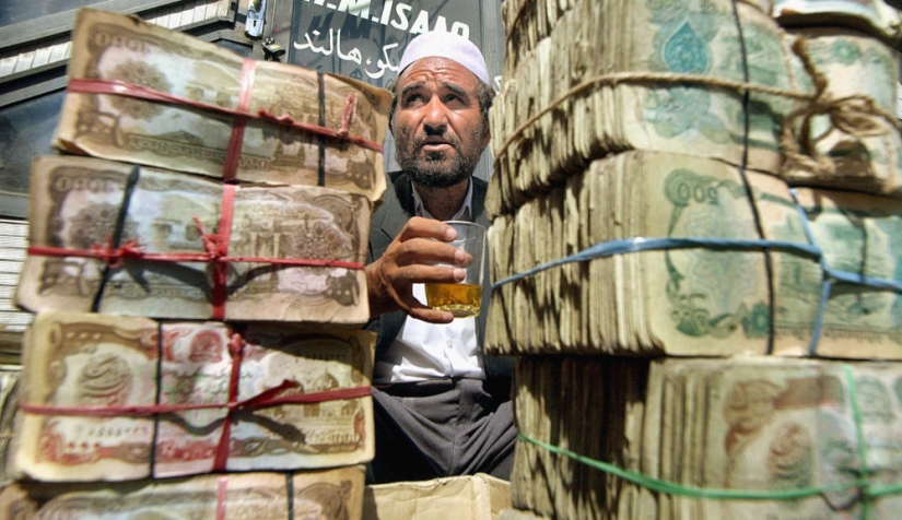 صراف أفغاني يدعى عبد العزيز يأخذ قسطًا من الراحة بينما يجلس خلف مجموعات من أوراق العملة الأفغانية في سوق الصرف الرئيسي في كابول، في 18 تموز/ يوليو 2002.