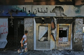 شاب يسير أمام فرع محترق لبنك "Blom" في ميدان النور بمدينة طرابلس