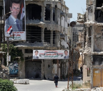 لافتات تحمل صورة الرئيس بشار الأسد تتدلى من المباني التي دمرتها المعارك في مدينة حمص.