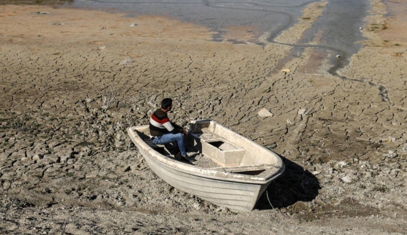 رجل يجلس في قارب حيث كانت بحيرة الدويسات قبل أن تجف عند سد الدويسات في إدلب