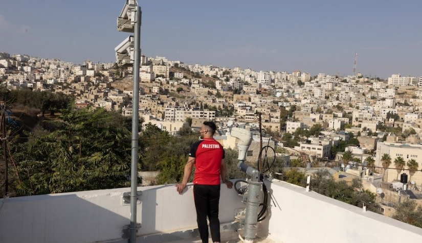 فلسطيني يقف بجانب كاميرات مراقبة وضعها الجيش الإسرائيلي على سطح إحدى البنايات في مدينة الخليل بالضفة الغربية، في 13 تشرين الأول/ أكتوبر سنة 2021.