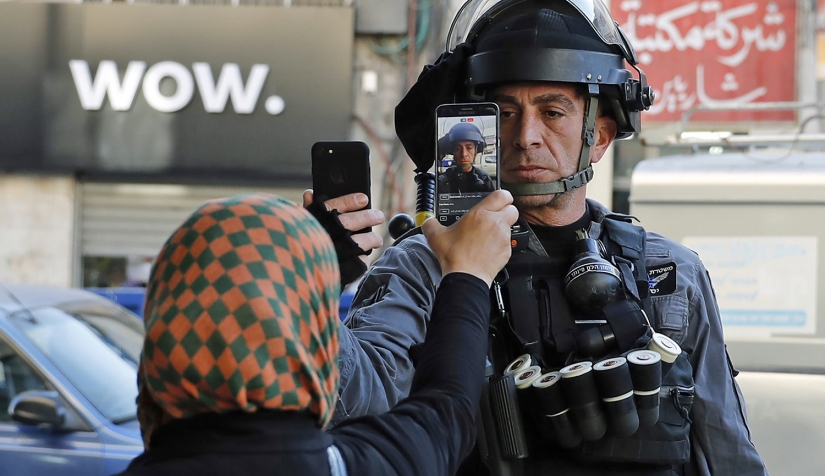 فلسطينية تلتقط صورة لأحد أفراد قوات الأمن الإسرائيلية الذي كان بصدد التقاط صورة لها دون إذن في أحد شوارع القدس، 16 كانون الأول/ ديسمبر 2017. 