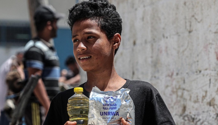 صبي يحمل زجاجة زيت وعبوة حليب من وكالة الأمم المتحدة للاجئين الفلسطينيين في غزة.