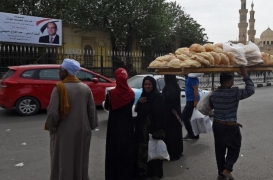 بائع خبز يمشي أمام ملصق للرئيس السيسي عند جامع الأزهر وسط القاهرة