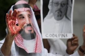 متظاهر يرتدي قناعًا كأنه ابن سلمان ويده مخضبة بالدماء أمام السفارة السعودية في واشنطن 2018