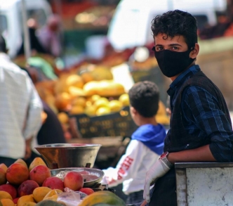 شاب يمني يرتدي قناعًا واقيًا وهو يبيع الفاكهة في أحد شوارع تعز