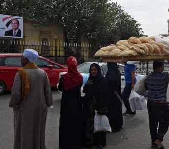 بائع خبز يمشي أمام ملصق للرئيس السيسي عند جامع الأزهر وسط القاهرة