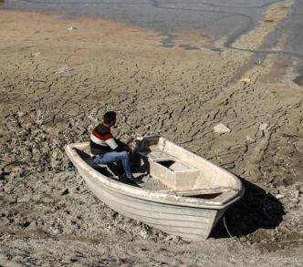 رجل يجلس في قارب حيث كانت بحيرة الدويسات قبل أن تجف عند سد الدويسات في إدلب