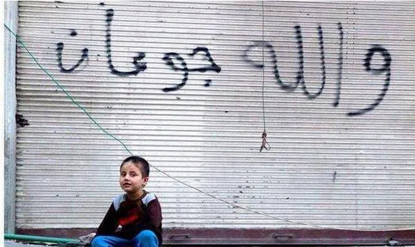 طفل-سوري-وكتب-خلفه-عبارة-تدل-على-سوء-أحوالهم-جراء-الحصار-المفروض-على-مخيم-اليرموك