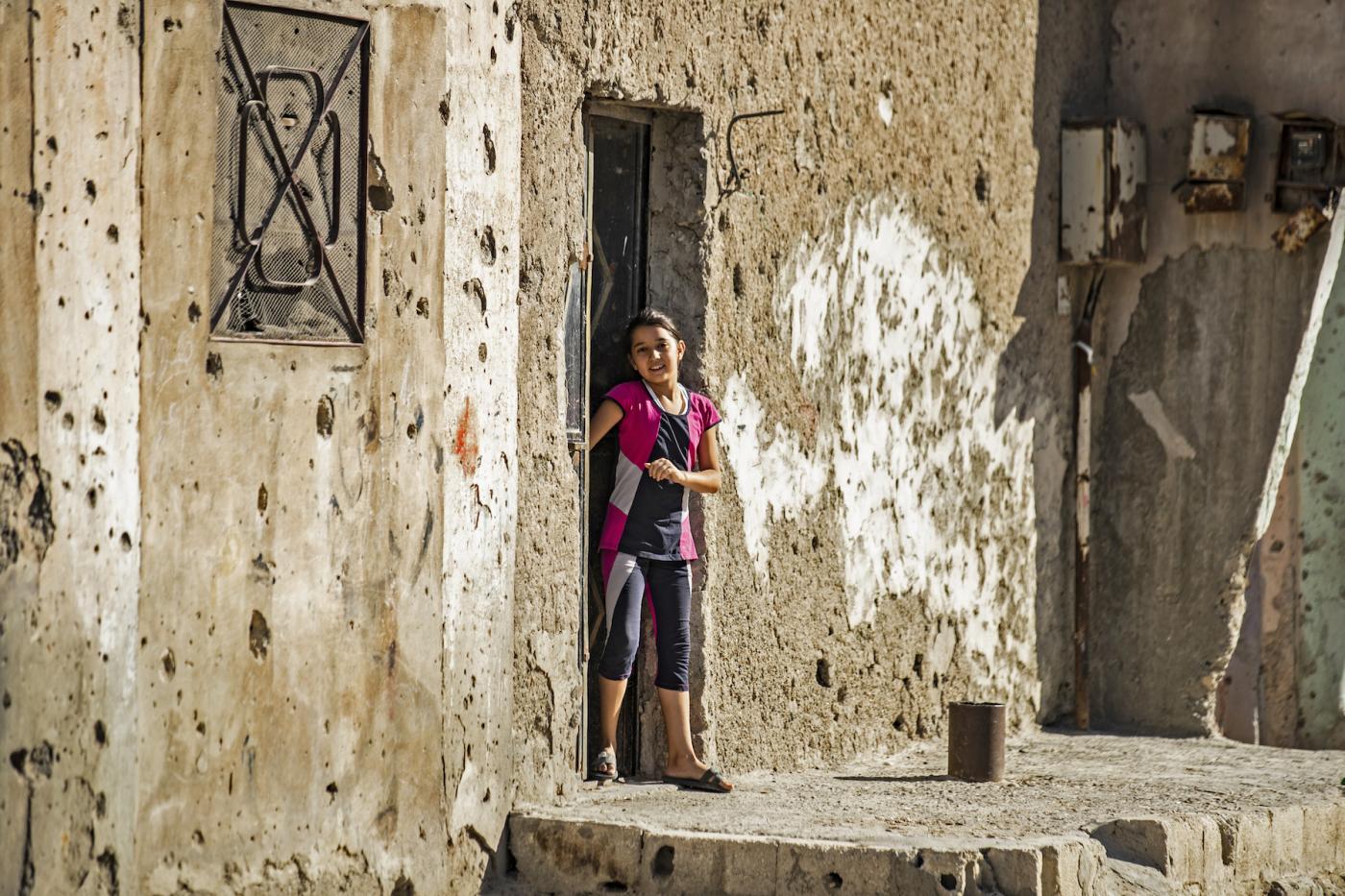 طفلة تقف بجوار جدار منزل مثقوب بالرصاص في الرقة