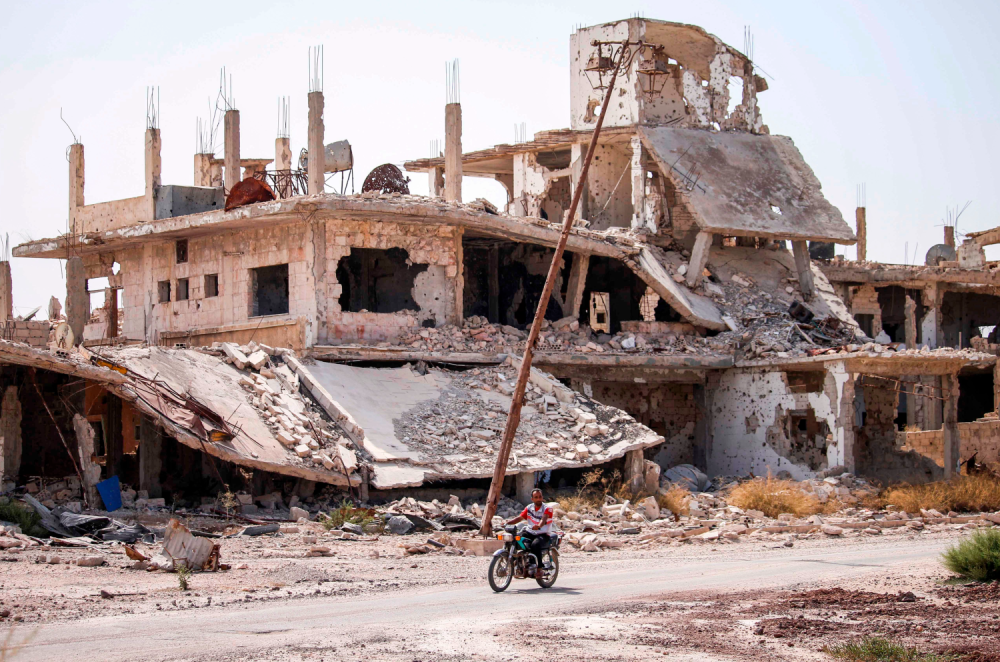 رجل على متن دراجة نارية يمر بجانب منازل مدمرة في حي تسيطر عليه المعارضة في مدينة درعا جنوب سوريا.