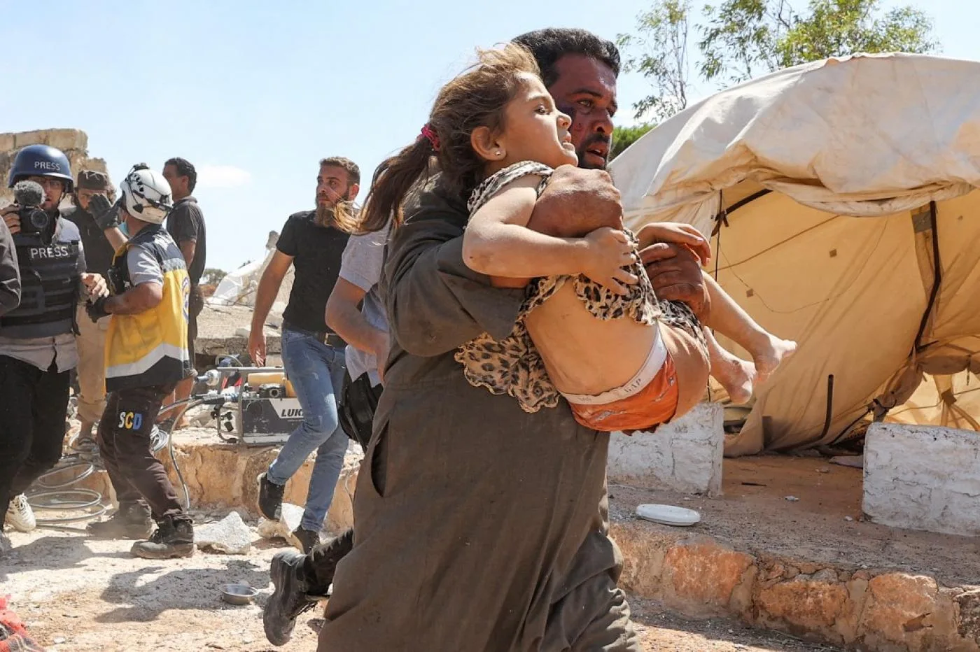 رجل يحمل فتاة أُصيبت في أثناء قصف جوي لمخيم مؤقت للنازحين قرب بلدة كفريا