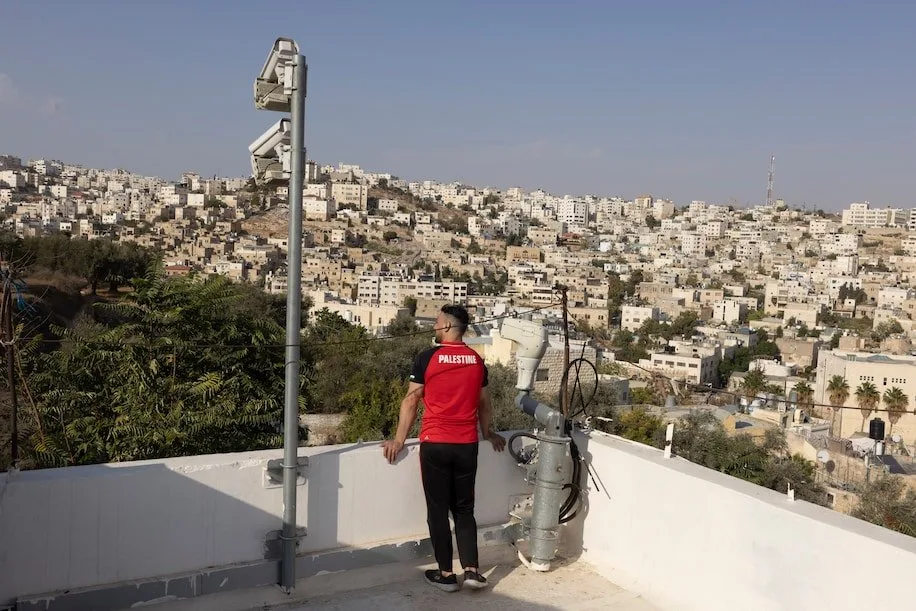 فلسطيني يقف بجانب كاميرات مراقبة وضعها الجيش الإسرائيلي على سطح إحدى البنايات في مدينة الخليل بالضفة الغربية، في 13 تشرين الأول/ أكتوبر سنة 2021.