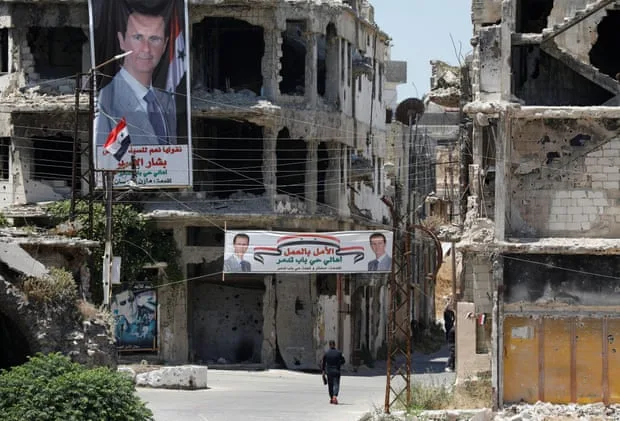 لافتات تحمل صورة الرئيس بشار الأسد تتدلى من المباني التي دمرتها المعارك في مدينة حمص.