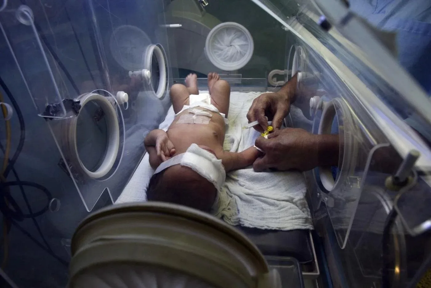 ممرضة فلسطينية تقدم الرعاية الطبية لطفل حديث الولادة في حاضنة بمستشفى الشفاء في غزة.