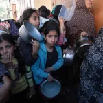 فلسطينيون يحملون أوعية فارغة ينتظرون توزيع المواد الغذائية من قبل متطوعين في نقطة مساعدات إنسانية في دير البلح بغزة، في 26 كانون الثاني/يناير 2024.